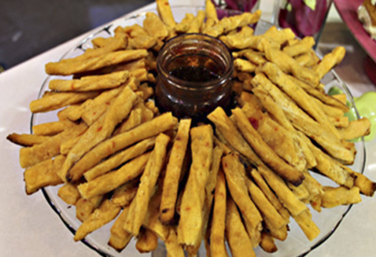 Artfully plated golden-fried cheese straws arranged in a sunburst pattern with dark dipping sauce, ideal for wholesale food service and catering operations.